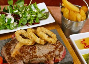 A image of a black rock grill lava stone rock cooking steak with onion rings.